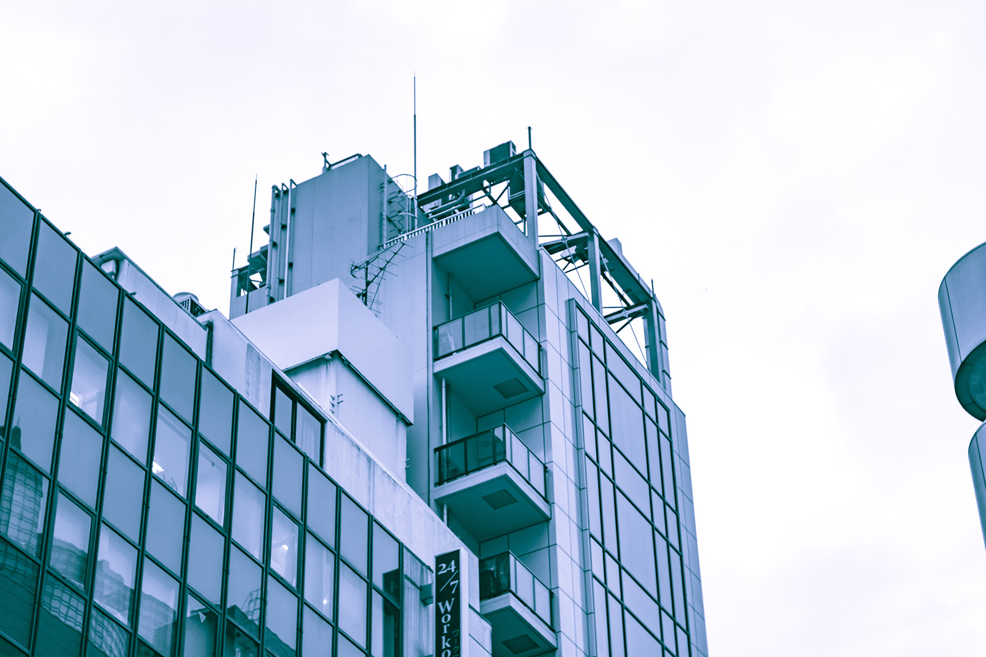 Low-contrast blue-tinted view of a rooftop of a glass and modern concrete building, seen from below.